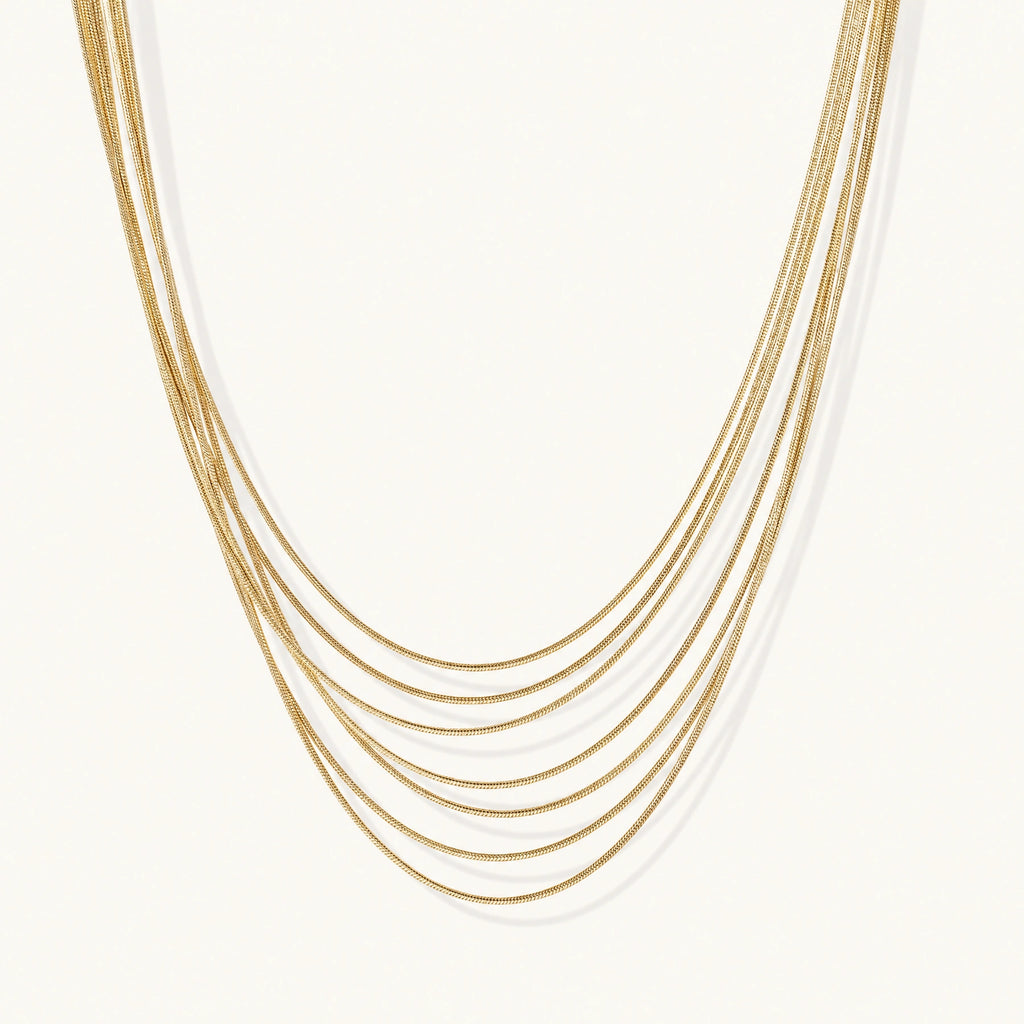 Seven delicate gold-plated snake chains create an elegant layered necklace on a neutral background.
