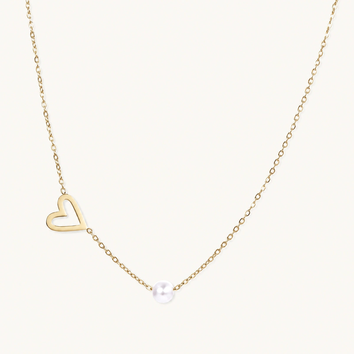 Dainty 14K gold plated stainless steel necklace with an open heart charm and a single round white bead on a cream background.