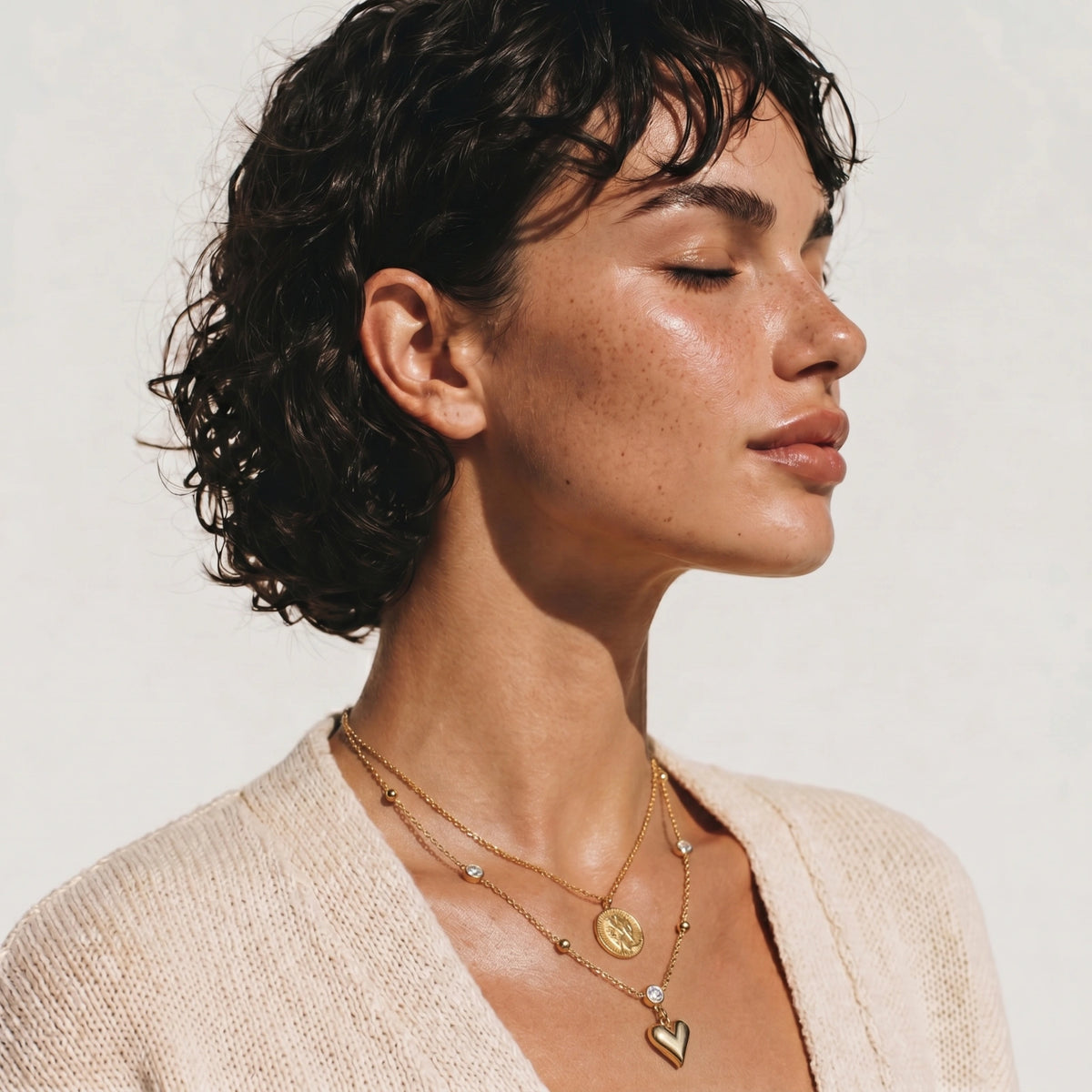 Delicate gold-plated necklace with bezel-set crystals and small heart pendant on beige background