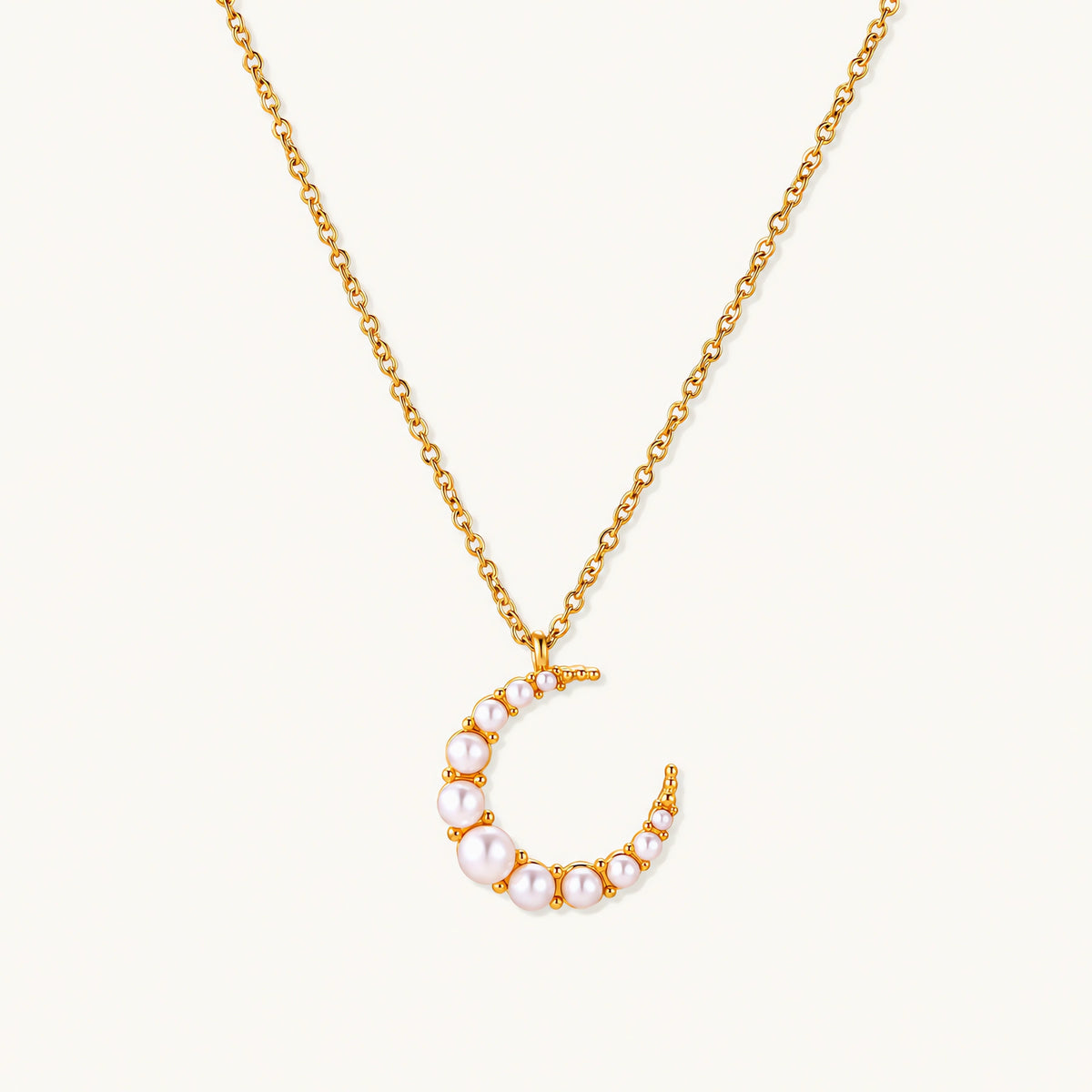 Gold crescent moon pendant with graduated white pearls on delicate chain against cream background