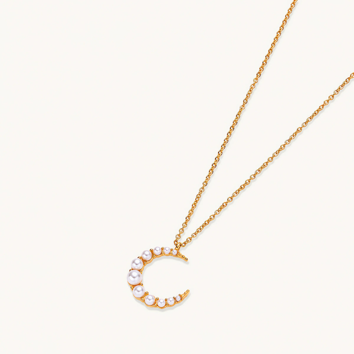 Gold crescent moon pendant with graduated white pearls on delicate chain against cream background