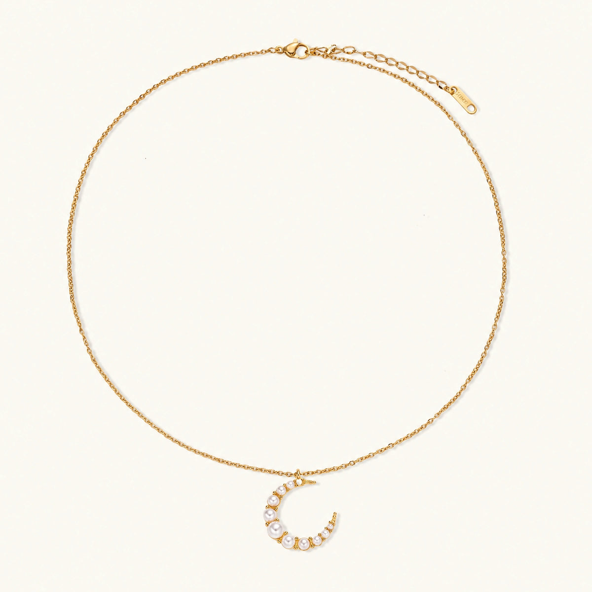 Gold crescent moon pendant with graduated white pearls on delicate chain against cream background