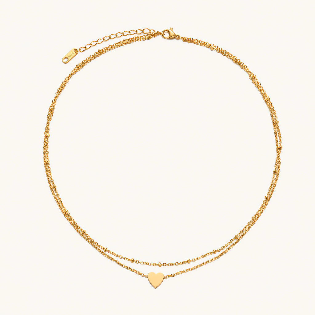 Delicate double-chain gold necklace with tiny heart pendant on cream background