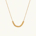 Delicate gold-plated necklace with graduated spherical beads forming gentle smile curve on beige background