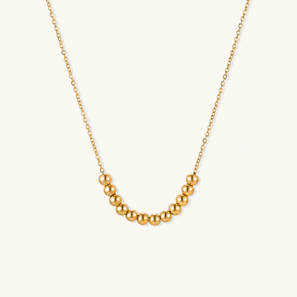 Delicate gold-plated necklace with graduated spherical beads forming gentle smile curve on beige background