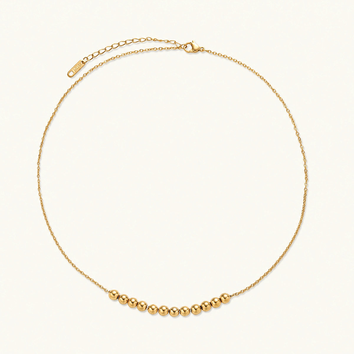 Delicate gold-plated necklace with graduated spherical beads forming gentle smile curve on beige background