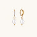 Gold huggie hoop earrings with pavé crystals and white freshwater pearl drops on cream background