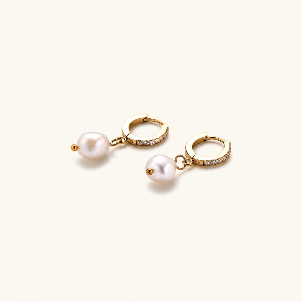 Gold huggie hoop earrings with pavé crystals and white freshwater pearl drops on cream background