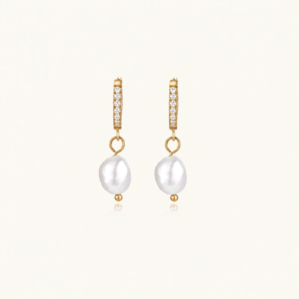 Gold huggie hoop earrings with pavé crystals and white freshwater pearl drops on cream background