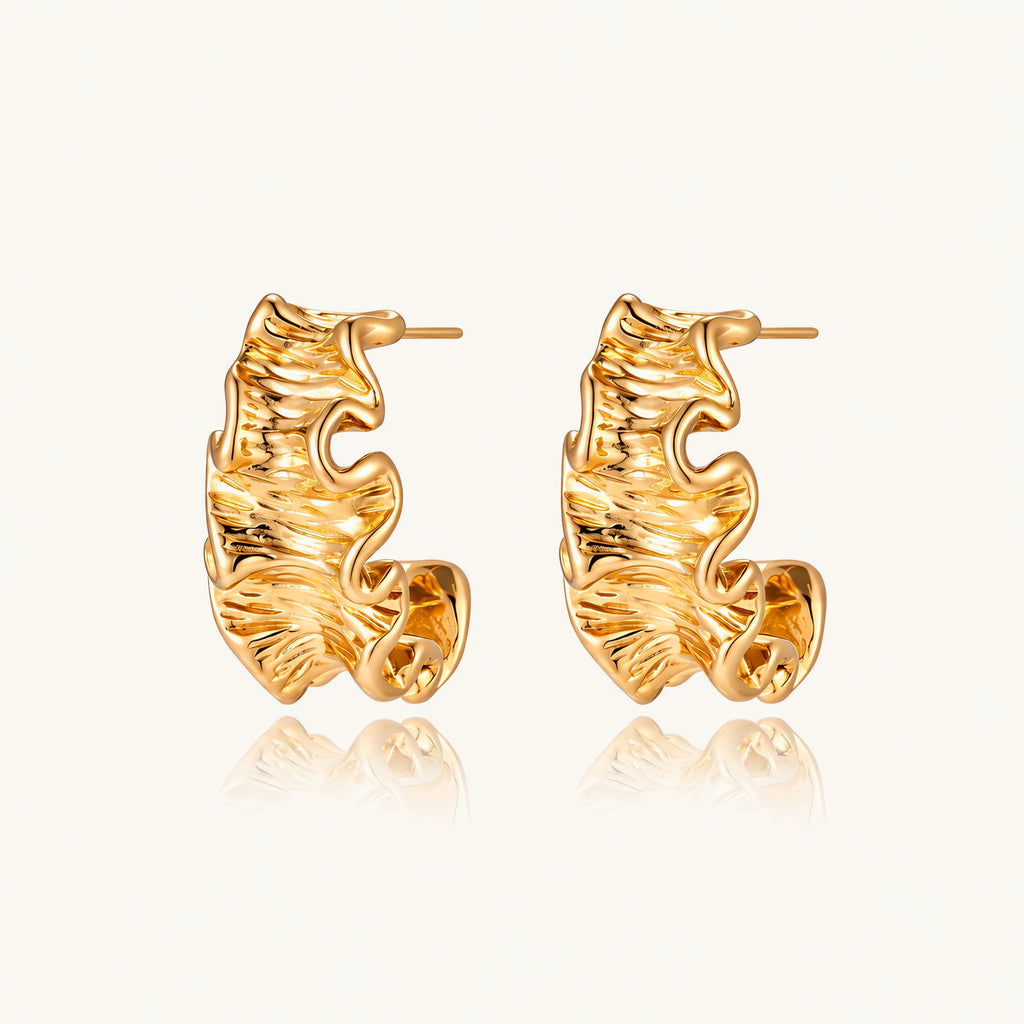 Pair of gold huggie hoops with sculpted wave texture and dimensional ripples on neutral background.