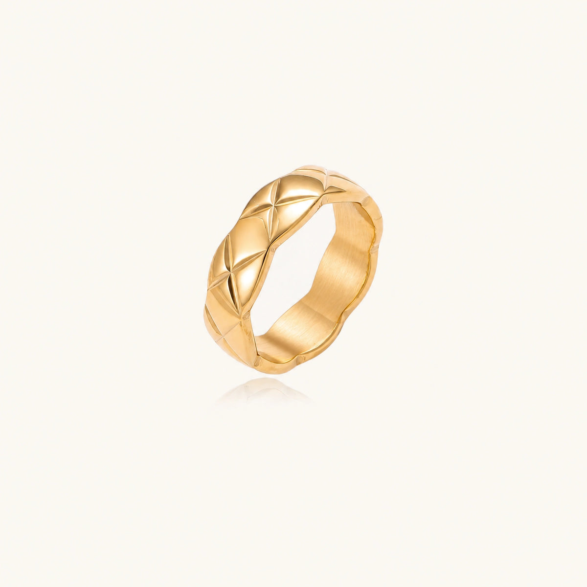 Close-up of an 18K gold-plated twisted band ring with dimensional braided pattern on cream background.