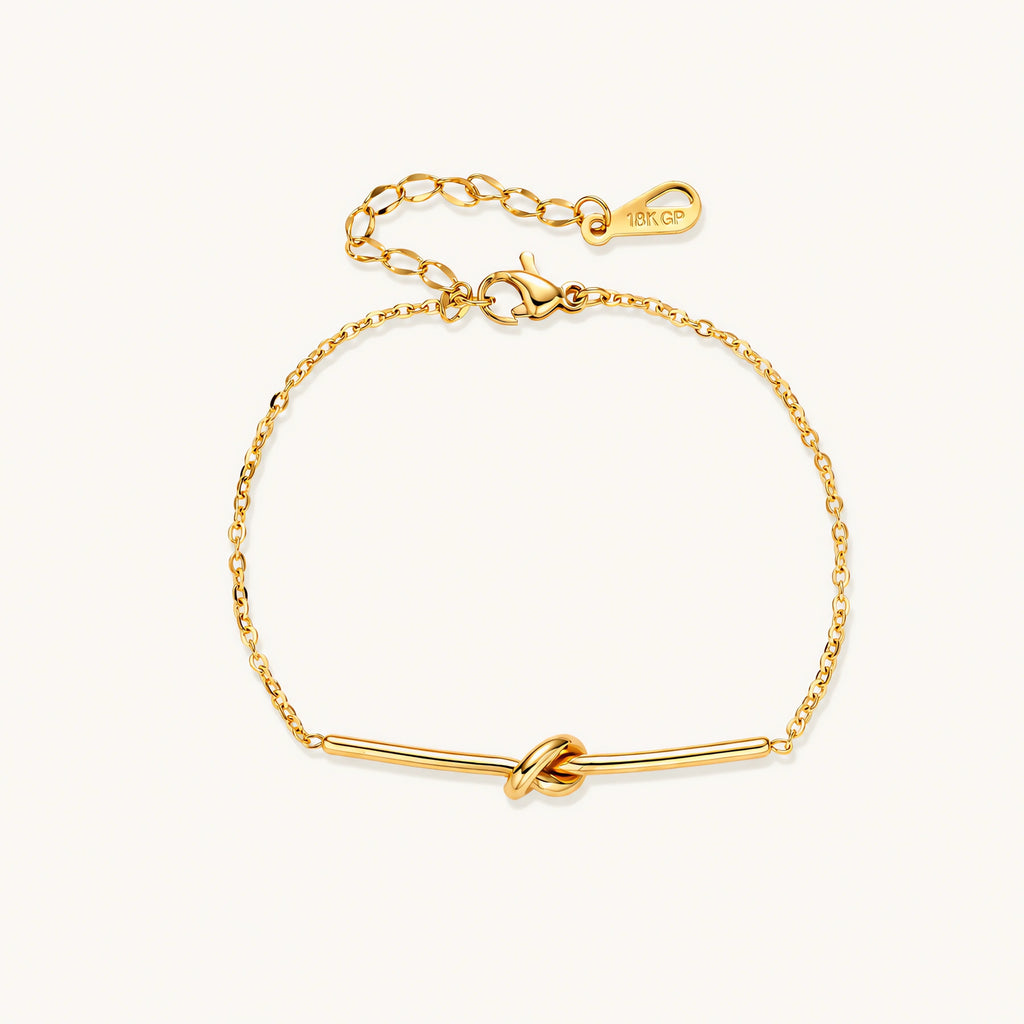 Delicate gold chain bracelet with minimalist bar and centered knot detail on cream background