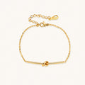 Delicate gold chain bracelet with minimalist bar and centered knot detail on cream background