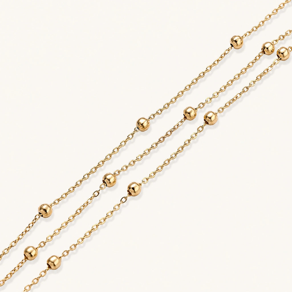 Three-strand gold-plated bracelet with clustered ball beads and adjustable clasp on cream background