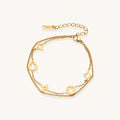 Double-layer gold-plated bracelet with quatrefoil and star charms on cream background, 18K gold finish.
