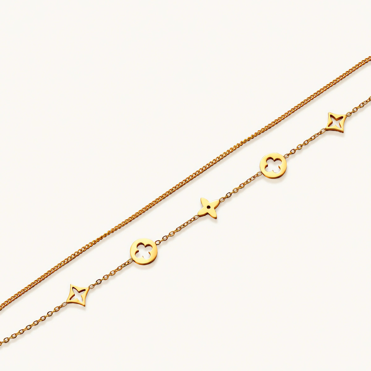 Double-layer gold-plated bracelet with quatrefoil and star charms on cream background, 18K gold finish.