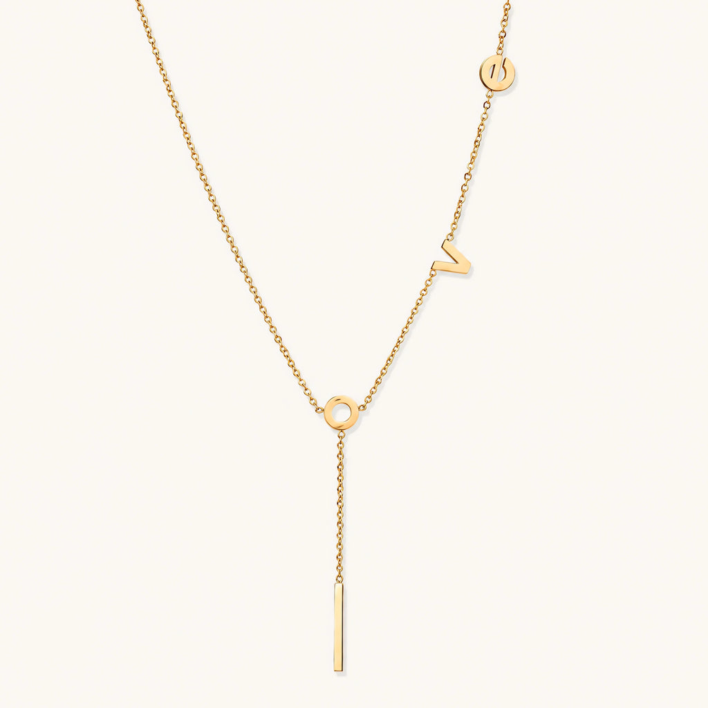 Gold Y-shaped necklace with L-O-V-E letter charms and vertical bar pendant on delicate chain against cream background