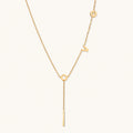 Gold Y-shaped necklace with L-O-V-E letter charms and vertical bar pendant on delicate chain against cream background