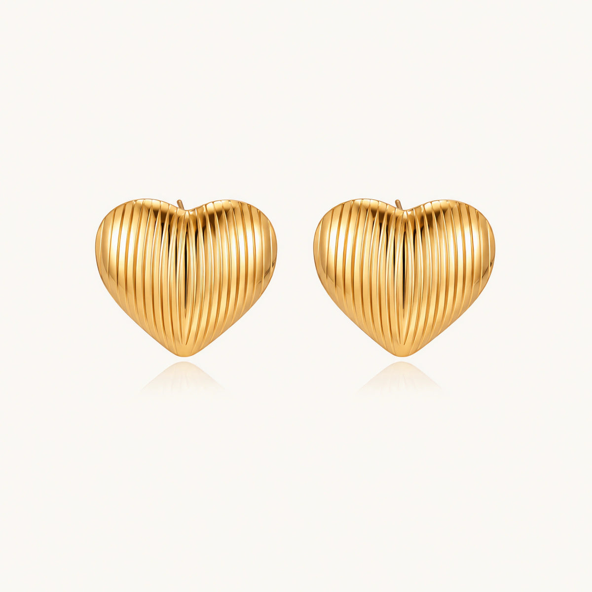 Gold heart-shaped stud earrings with parallel ridged texture on cream background