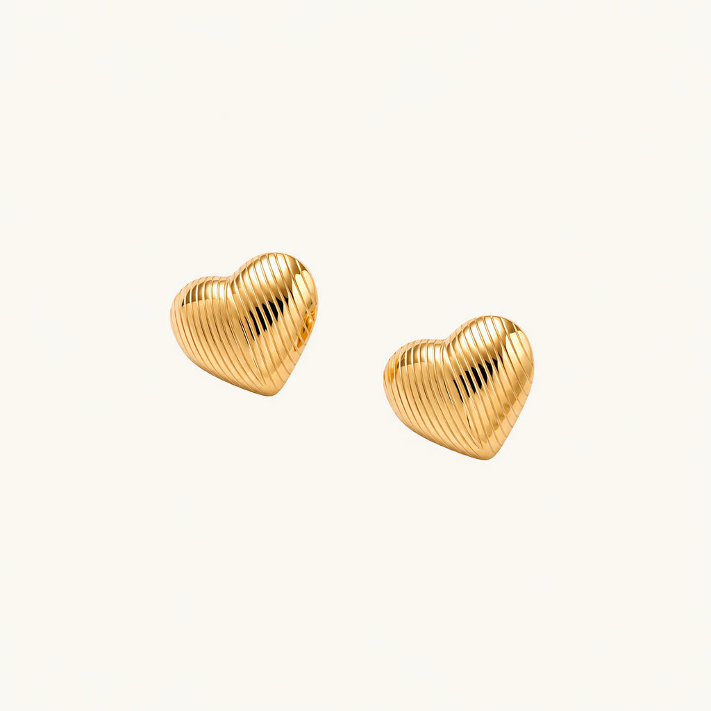 Gold heart-shaped stud earrings with parallel ridged texture on cream background