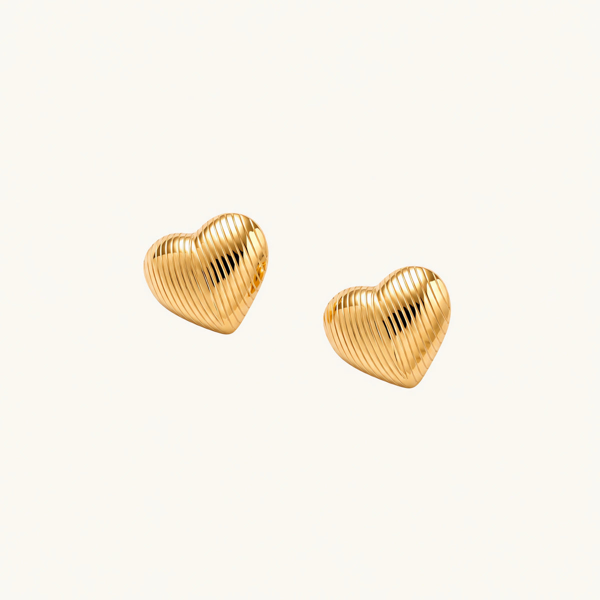 Gold heart-shaped stud earrings with parallel ridged texture on cream background