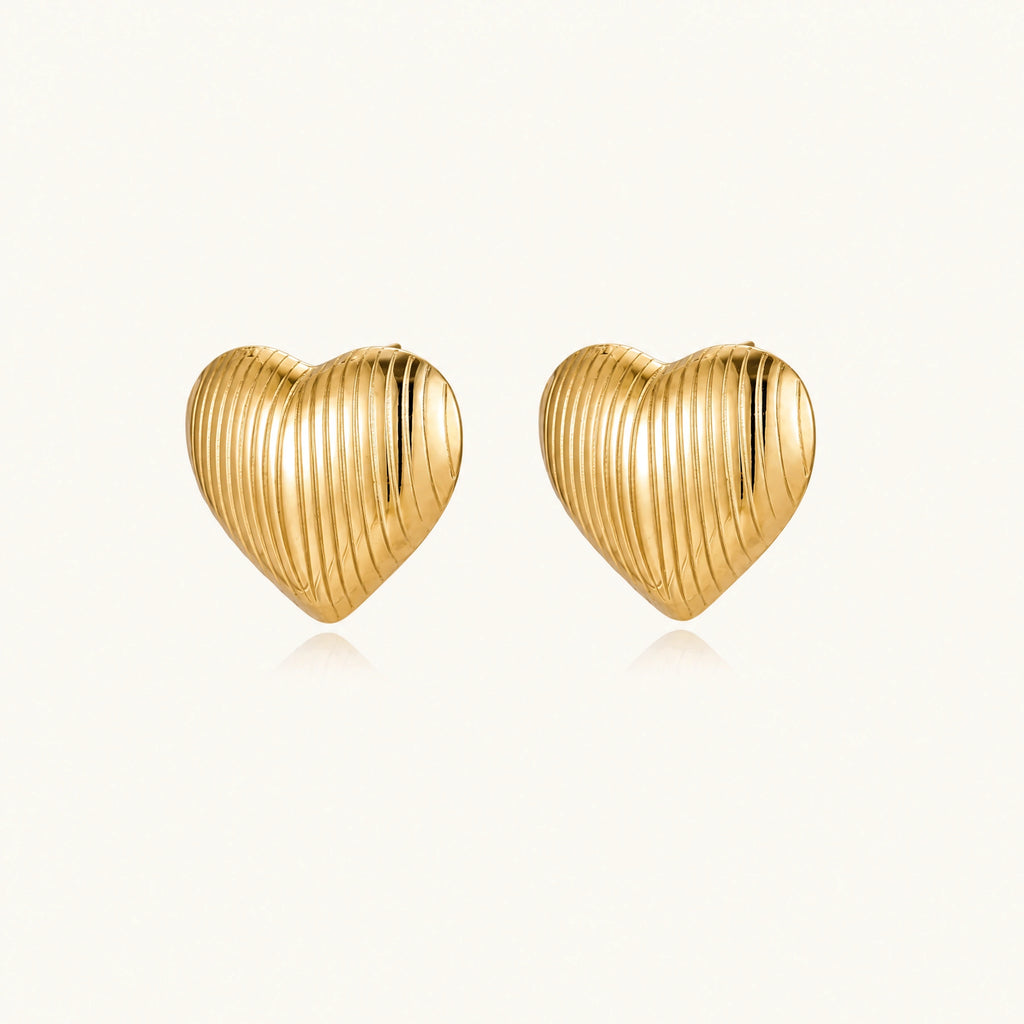 Gold heart-shaped stud earrings with parallel ridged texture on cream background