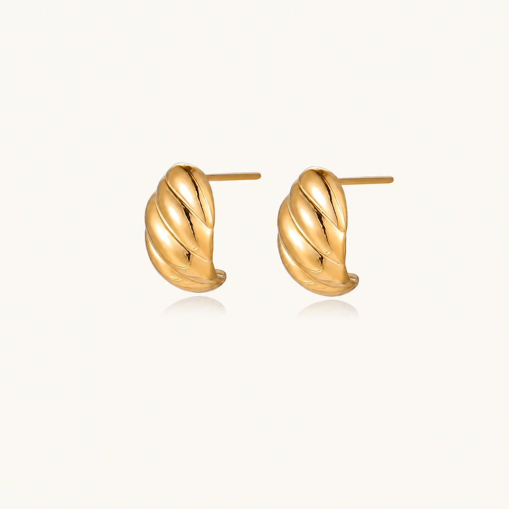 Chunky gold twisted rope huggie hoops with diagonal grooves and high-polish finish on cream background
