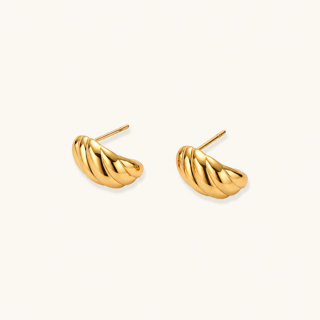 Chunky gold twisted rope huggie hoops with diagonal grooves and high-polish finish on cream background
