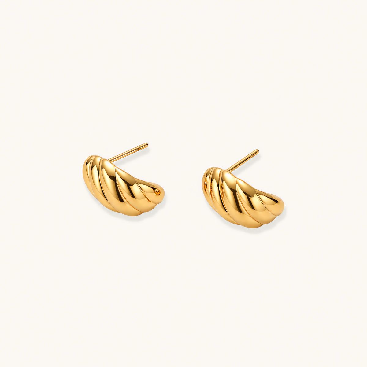Chunky gold twisted rope huggie hoops with diagonal grooves and high-polish finish on cream background