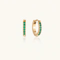 Pair of small gold huggie hoop earrings with bright green cubic zirconia stones on cream background