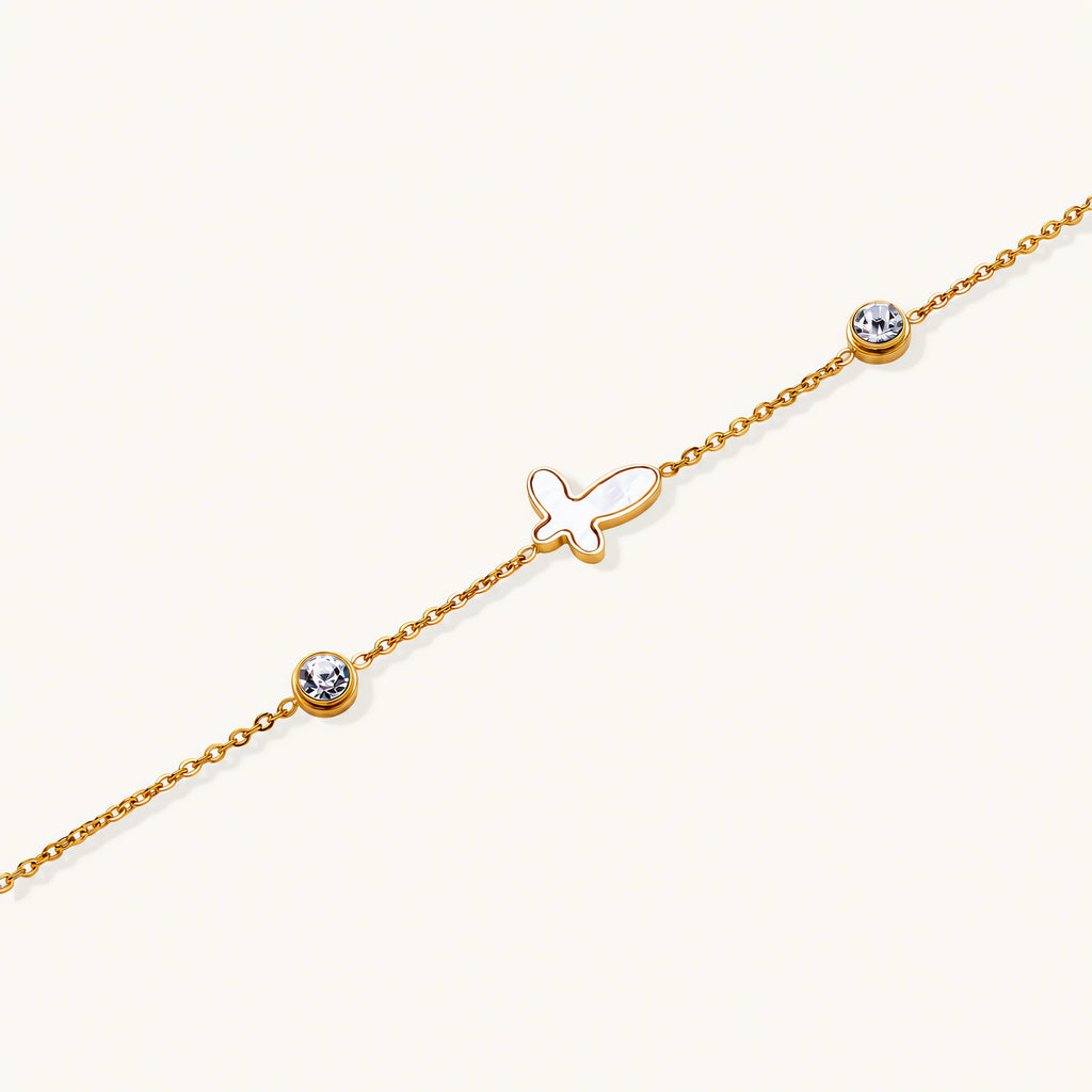Gold chain bracelet with white mother of pearl butterfly pendant and two bezel-set crystals on cream background
