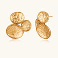 Three hammered gold discs clustered together forming organic statement earrings with textured surfaces