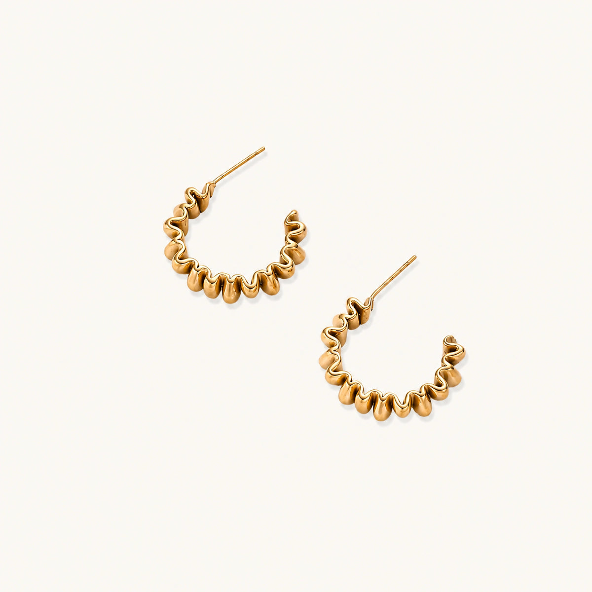 Sculptural gold-plated hoop earrings with continuous twisted spiral design on cream background