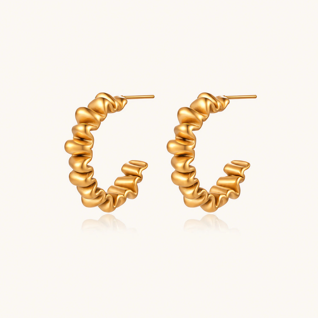 Sculptural gold-plated hoop earrings with continuous twisted spiral design on cream background