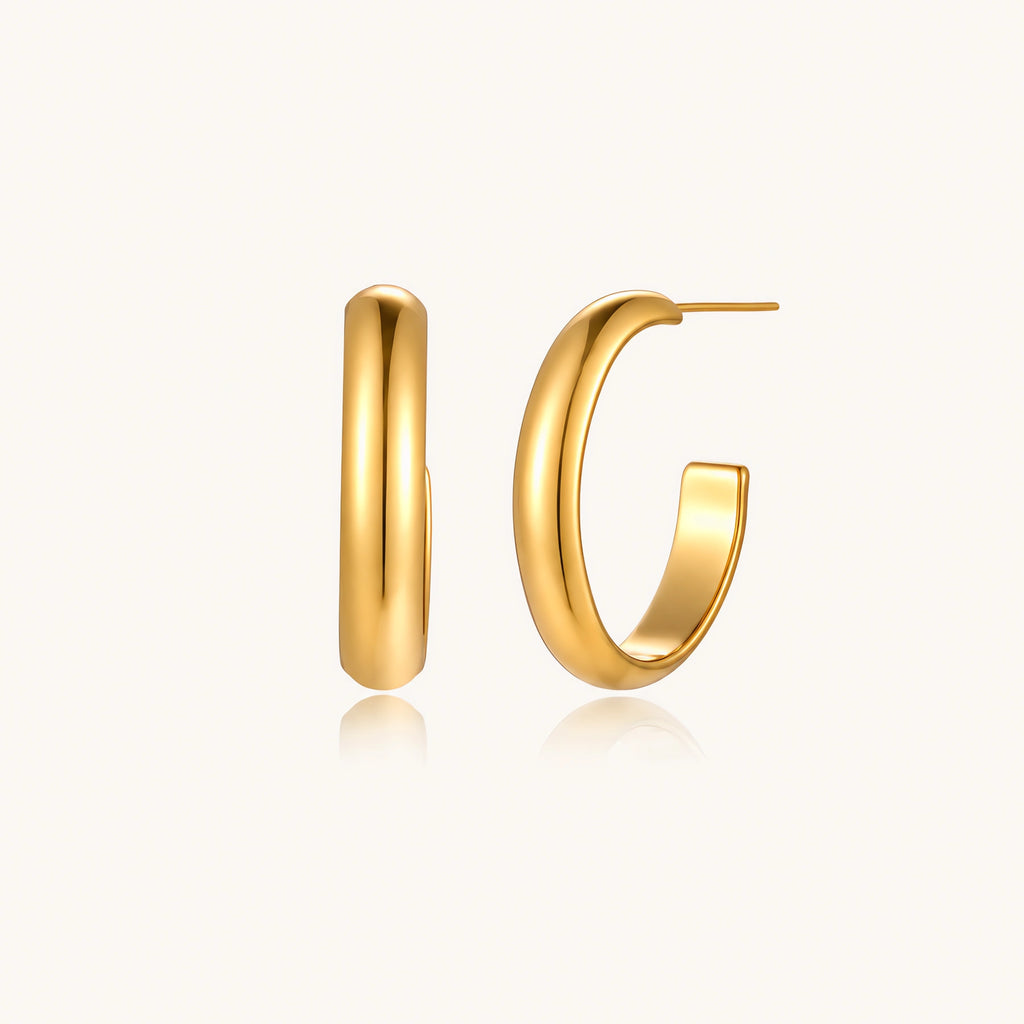 Chunky tubular hoop earrings in warm 14K gold-plated finish with smooth polished surface on cream background.