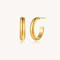 Chunky tubular hoop earrings in warm 14K gold-plated finish with smooth polished surface on cream background.