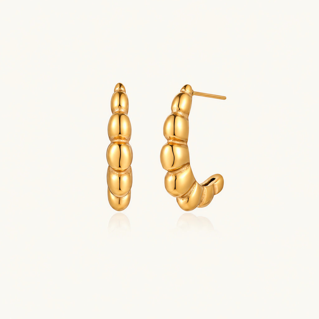 Gold-plated chunky hoop earrings with ridged bubble texture on cream background