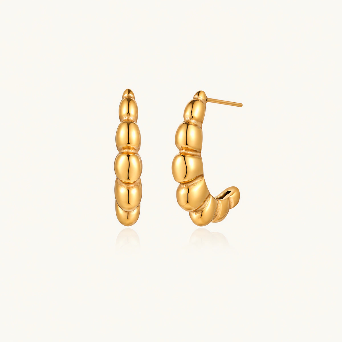Gold-plated chunky hoop earrings with ridged bubble texture on cream background