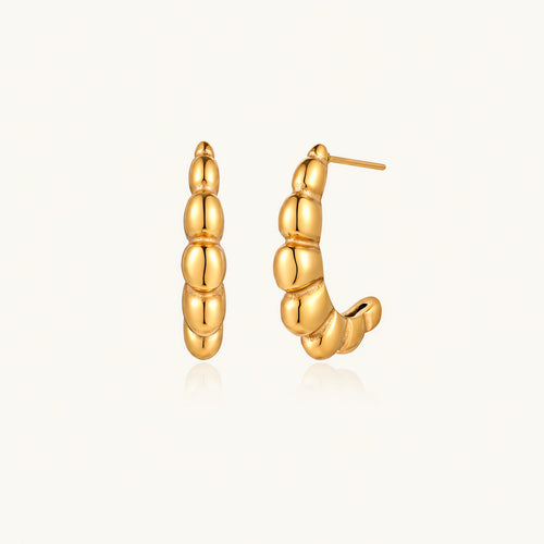 Gold-plated chunky hoop earrings with ridged bubble texture on cream background
