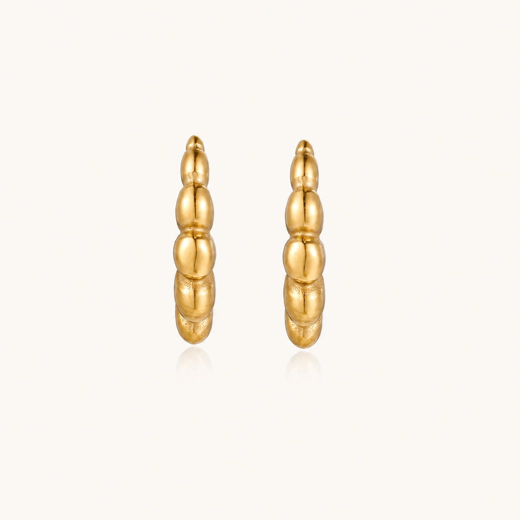 Gold-plated chunky hoop earrings with ridged bubble texture on cream background