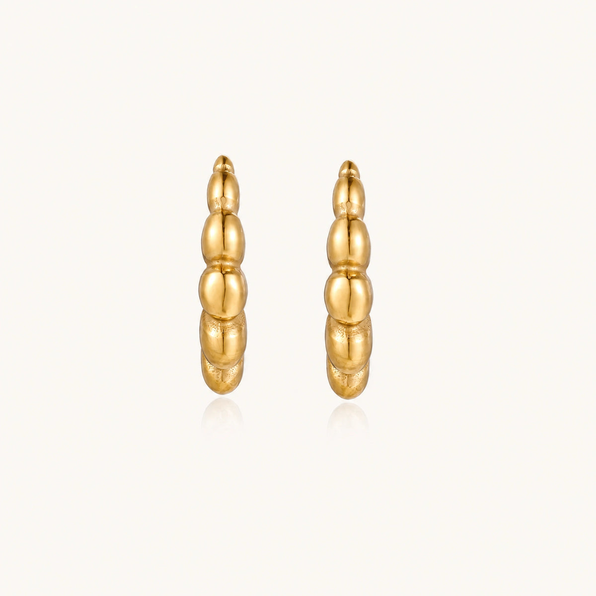 Gold-plated chunky hoop earrings with ridged bubble texture on cream background
