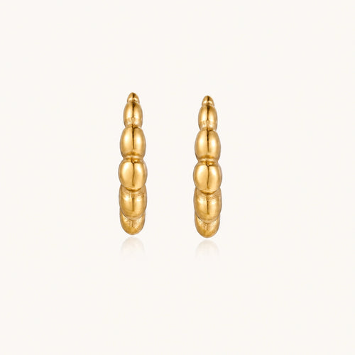 Gold-plated chunky hoop earrings with ridged bubble texture on cream background