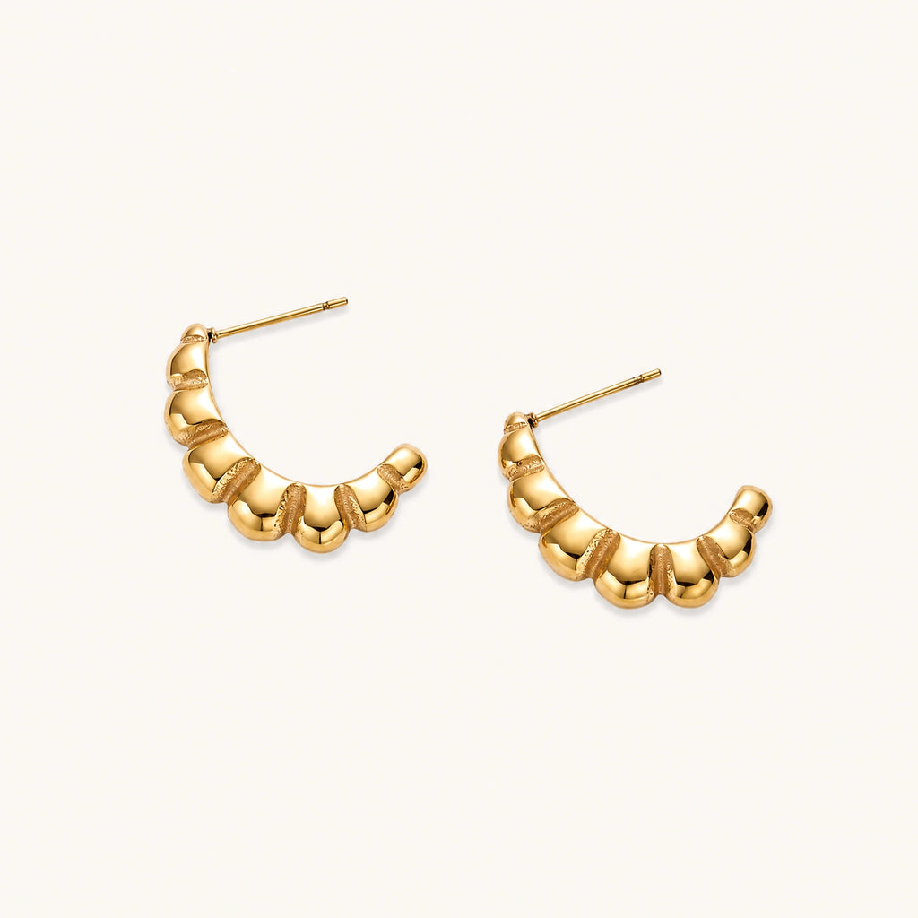 Gold-plated chunky hoop earrings with ridged bubble texture on cream background