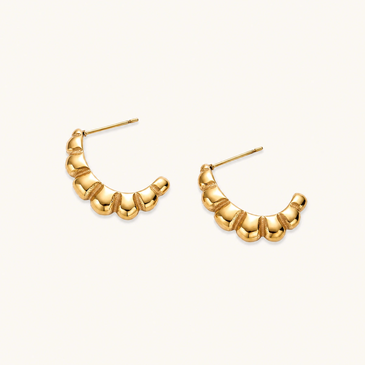 Gold-plated chunky hoop earrings with ridged bubble texture on cream background