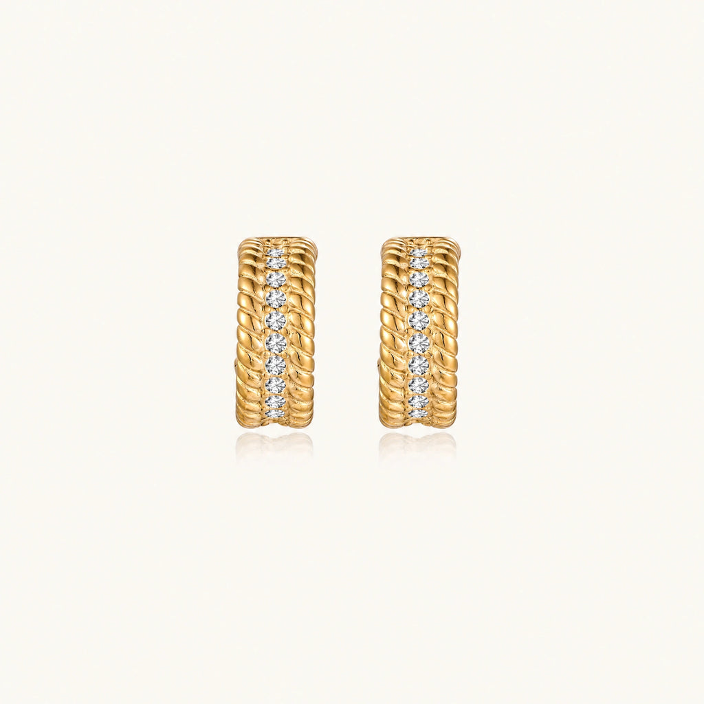 Textured gold huggie hoop earrings with raised ribbed rows creating dimensional sculptural design on cream background
