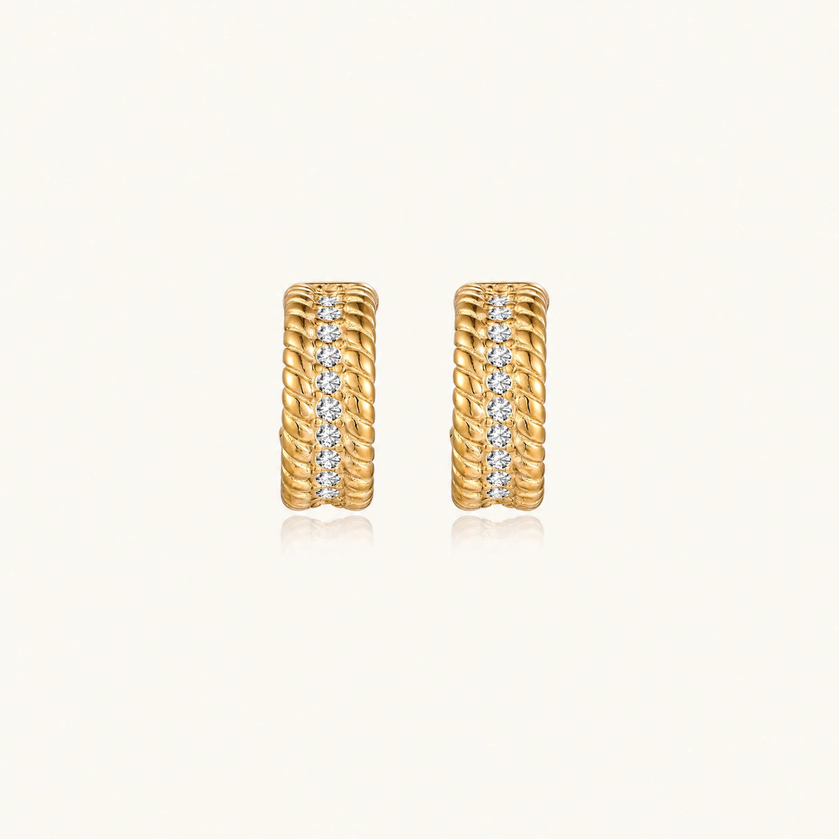 Textured gold huggie hoop earrings with raised ribbed rows creating dimensional sculptural design on cream background