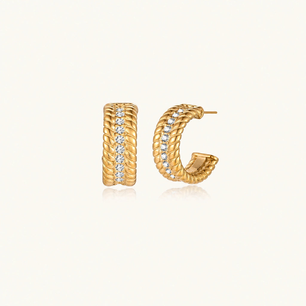 Textured gold huggie hoop earrings with raised ribbed rows creating dimensional sculptural design on cream background