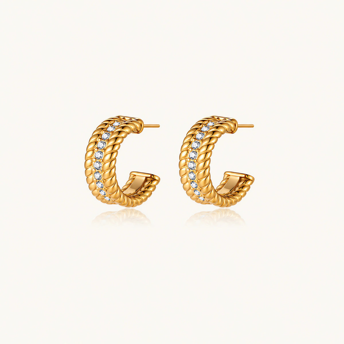 Textured gold huggie hoop earrings with raised ribbed rows creating dimensional sculptural design on cream background